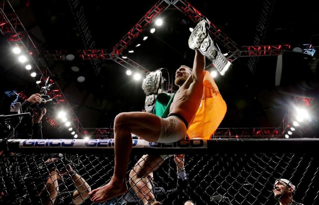 Two professional MMA fighters competing in the Octagon at UFC Perth 2026, Jack Della Maddalena performing a striking technique against Carlos Prates during UFC Fight Night, Official UFC Perth event poster featuring headlining fighters, Wide shot of the RAC Arena crowd during a UFC championship bout
